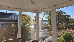 Un espacio exterior cubierto con luces colgantes, grandes ventanales que ofrecen vistas a una casa y paisajes naturales.