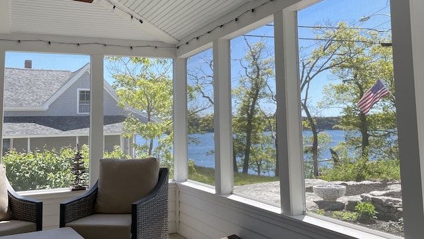 Una sala de estar con ventanales que dan a un lago, muebles de mimbre y una pequeña mesa.