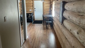 Een blokhutinterieur met een houten vloer, een eettafel met stoelen, een bank en een deur.