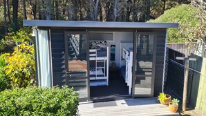 A modern, compact cabin with a sliding glass door entrance, a small deck, and two potted plants.