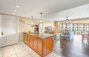 A modern kitchen with a central island, a dining area with a sofa and table, and a view of a multi-story building.
