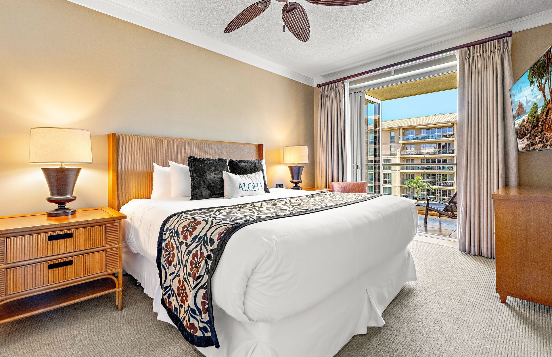 A hotel room with a large bed, two bedside tables with lamps, a wooden nightstand, a balcony with a view of the city, and a painting on the wall.