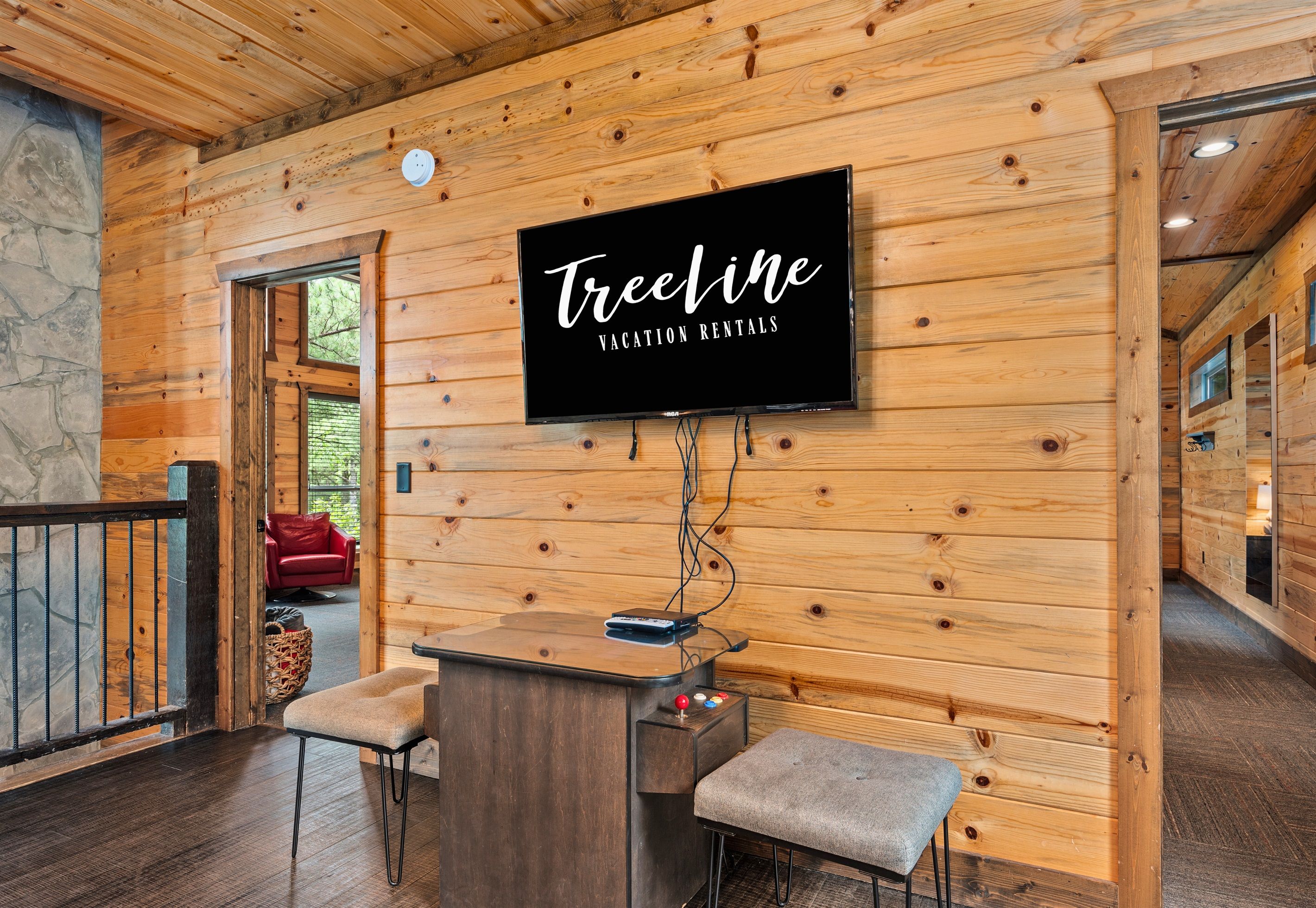 A wooden cabin interior with a mounted TV displaying "TreeLine Vacation Rentals".