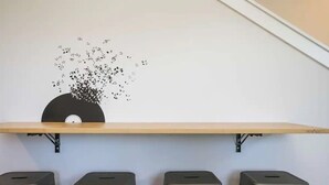 A wall-mounted shelf with a black circular object and a decorative black and white pattern. Below, there are four black stools aligned against the wall.