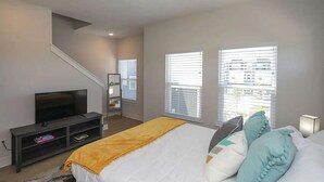 A bedroom with a bed, a TV, a window, and a staircase.