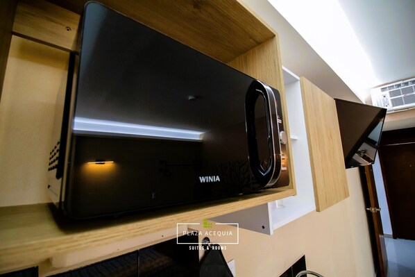Un refrigerador Winia negro en un mueble de madera, con el logotipo de Plaza Acequia Suites & Rooms a la vista.
