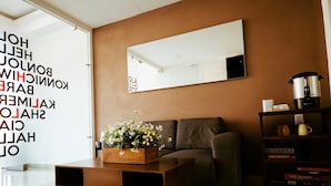 A modern living room with a sofa, a coffee table with flowers, a bookshelf, and a large mirror on the wall. - A06 SUPER CITY SUITE AT PLAZA ACEQUIA (Cuautitlan Izcalli)