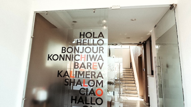 A modern hotel corridor with a glass wall displaying multilingual greetings, a staircase, and a clean, tiled floor. - A06 SUPER CITY SUITE AT PLAZA ACEQUIA (Cuautitlan Izcalli)