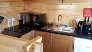 A wooden-paneled kitchen with a black countertop, stainless steel sink, and modern appliances including a microwave and toaster. - Harlosh Log Cabins, Cabin No 1 (Dunvegan)