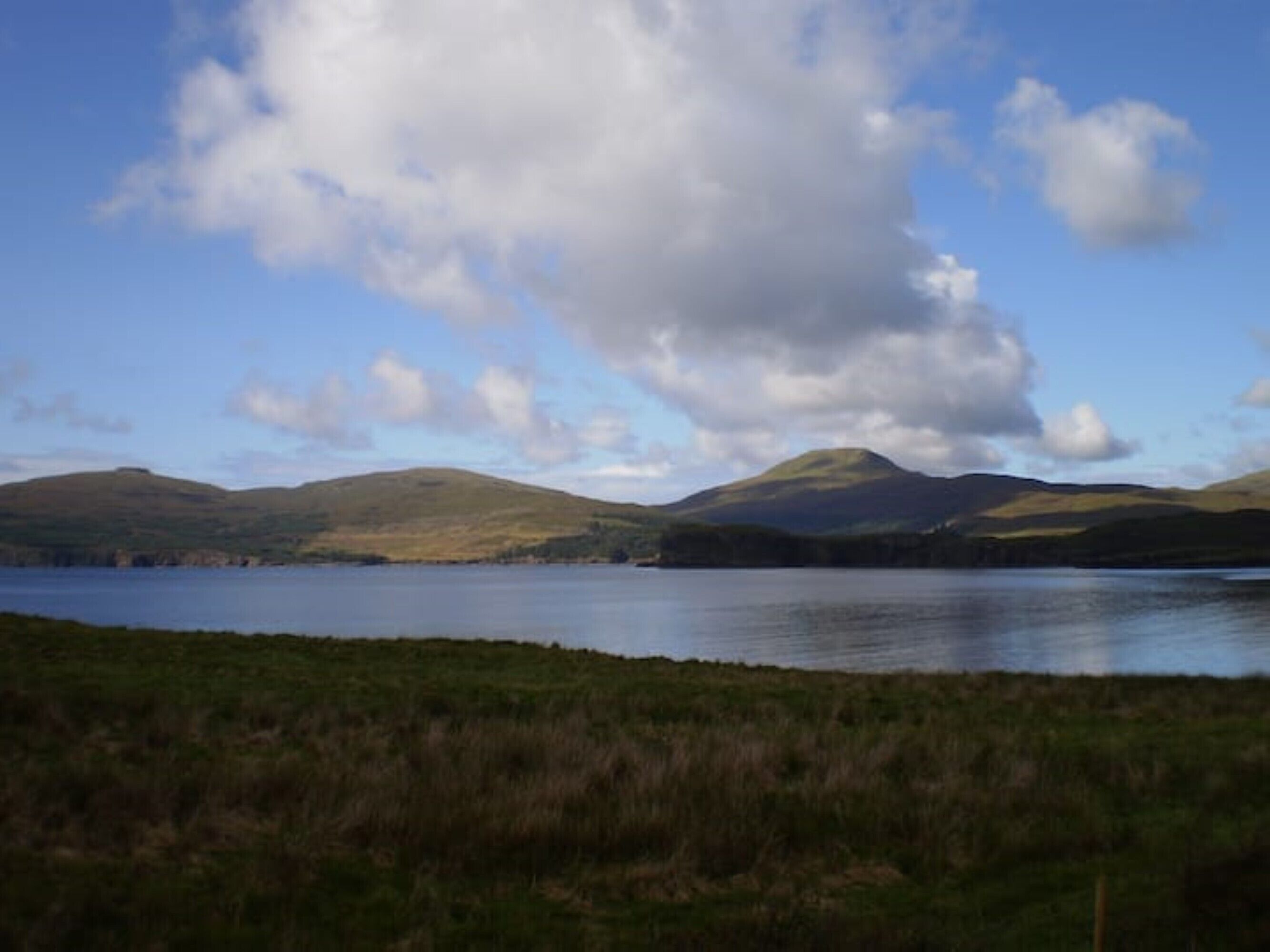A natural landscape with a lake, hills, and a partly cloudy sky.