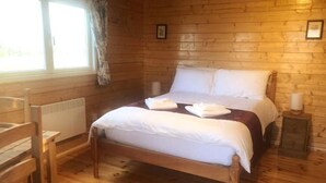 A wooden-paneled room with a bed, a chair, and a window. - Harlosh Log Cabins, Cabin No 1 (Dunvegan)