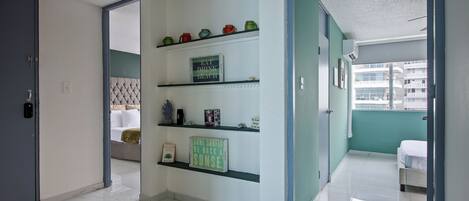 A hotel room with a bed, a shelf with decorative items, a door, and a view of the outside.