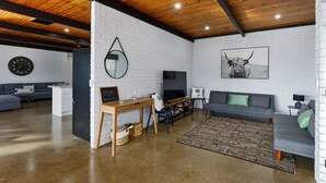 Un soggiorno moderno con soffitto in legno, un divano grigio, un tavolino da caffè e una televisione.