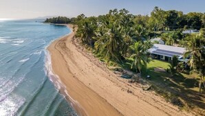 Una propiedad costera con playa arenosa, palmeras y una casa con techo blanco.