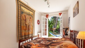 A bedroom with a large bed, a window with curtains, a view of greenery outside, and a wall tapestry. - Villa 'Familidy' with Private Pool, Wi-Fi and Air Conditioning (Bandol)