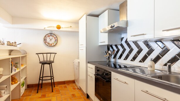 A compact kitchen with white cabinets, a black and white tiled backsplash, a stainless steel sink, and a clock on the wall. - Villa 'Familidy' with Private Pool, Wi-Fi and Air Conditioning (Bandol)
