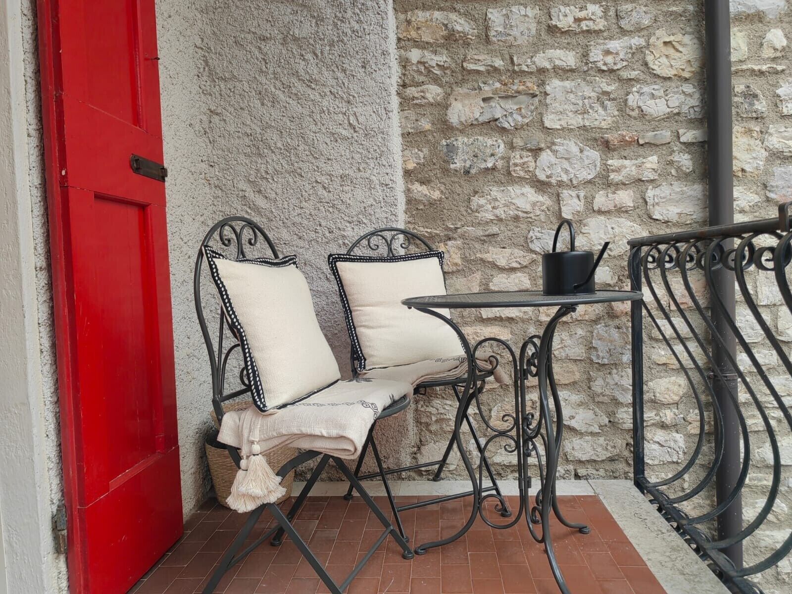 Une porte rouge, deux fauteuils rembourrés, une petite table et un mur en pierre.