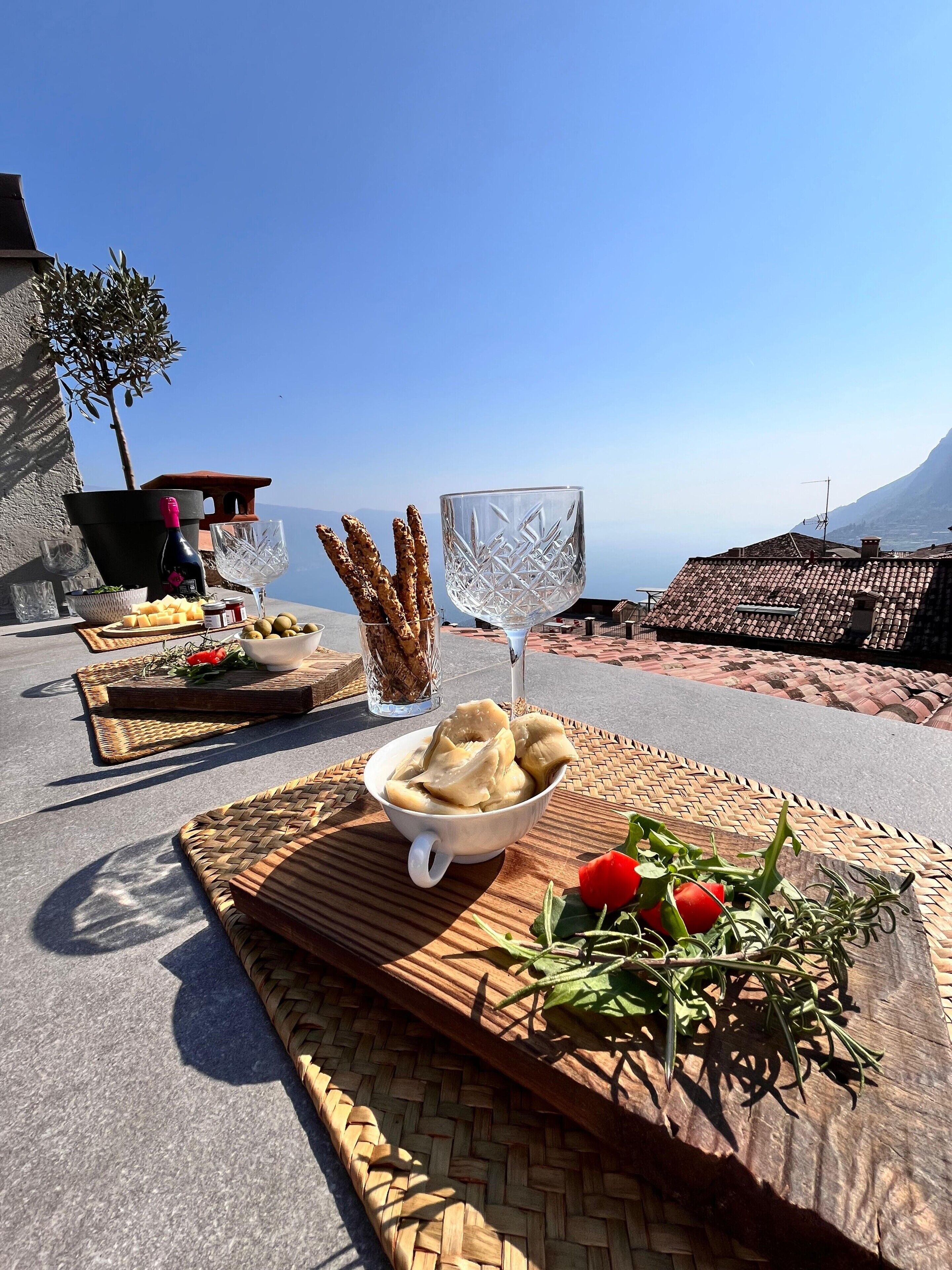 A table set with food and drinks, a view of the sea, and a mountain in the background.
