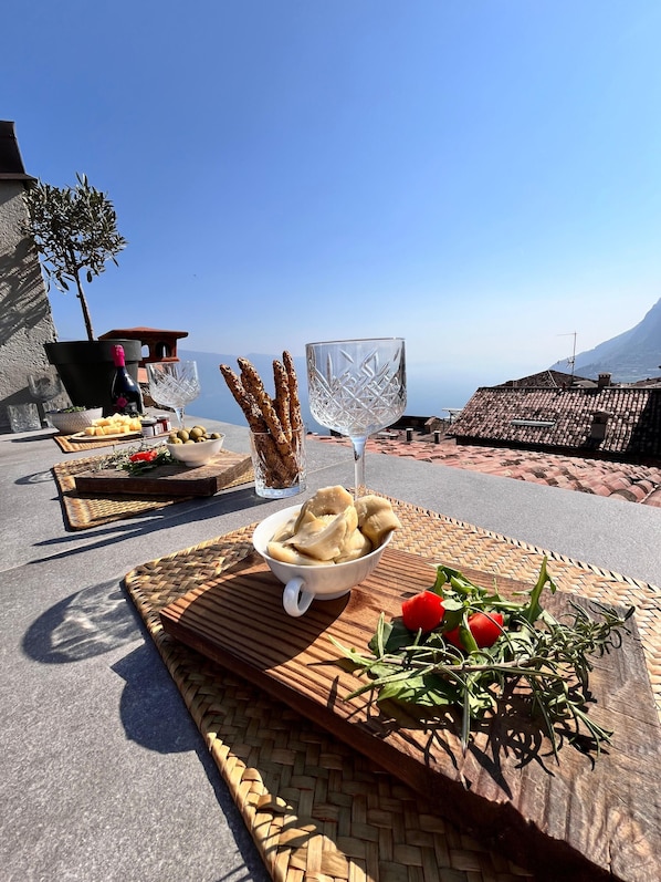 A table set with food and drinks, a view of the sea, and a mountain in the background.
