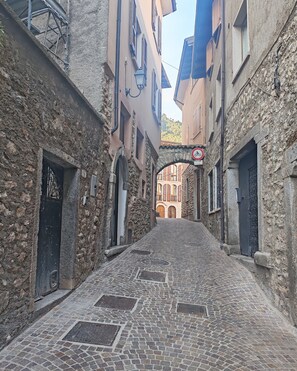 Une ruelle étroite pavée, bordée de bâtiments anciens en pierre, dotés d’entrées en arc de cercle et d’un panneau indiquant qu’il est interdit de se garer.