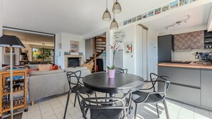 A modern kitchen with a dining area, a staircase, and a living room with a sofa and a TV.