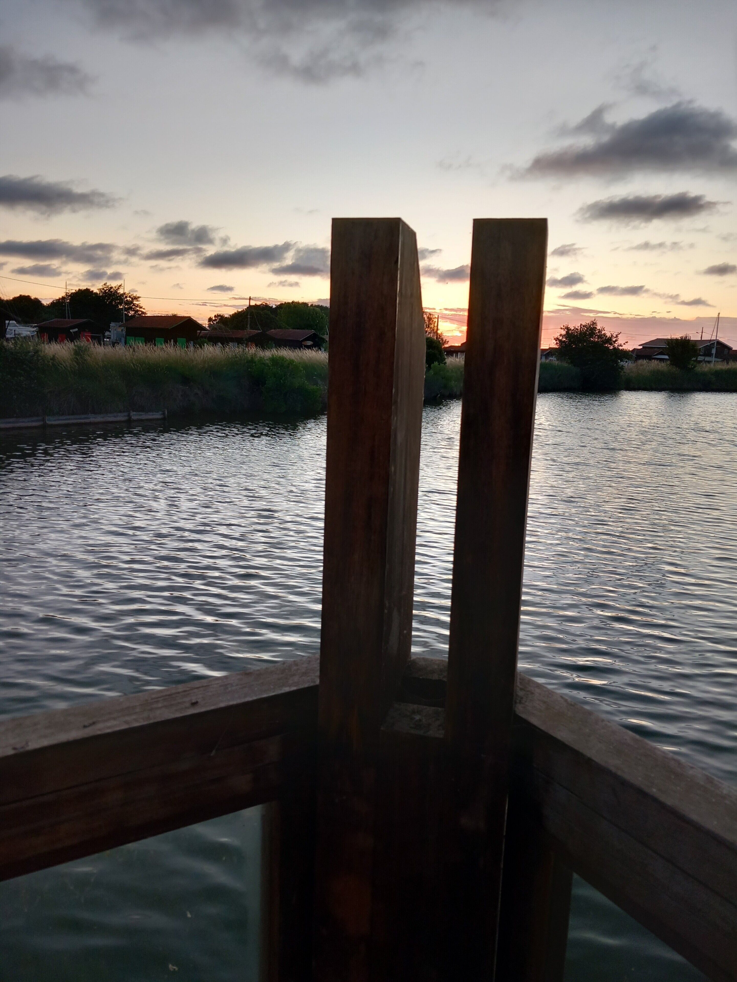 A wooden railing overlooking a calm body of water with a sunset in the background.