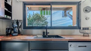A modern kitchen with a built-in dishwasher, a window with a view of trees, and a clock on the wall.