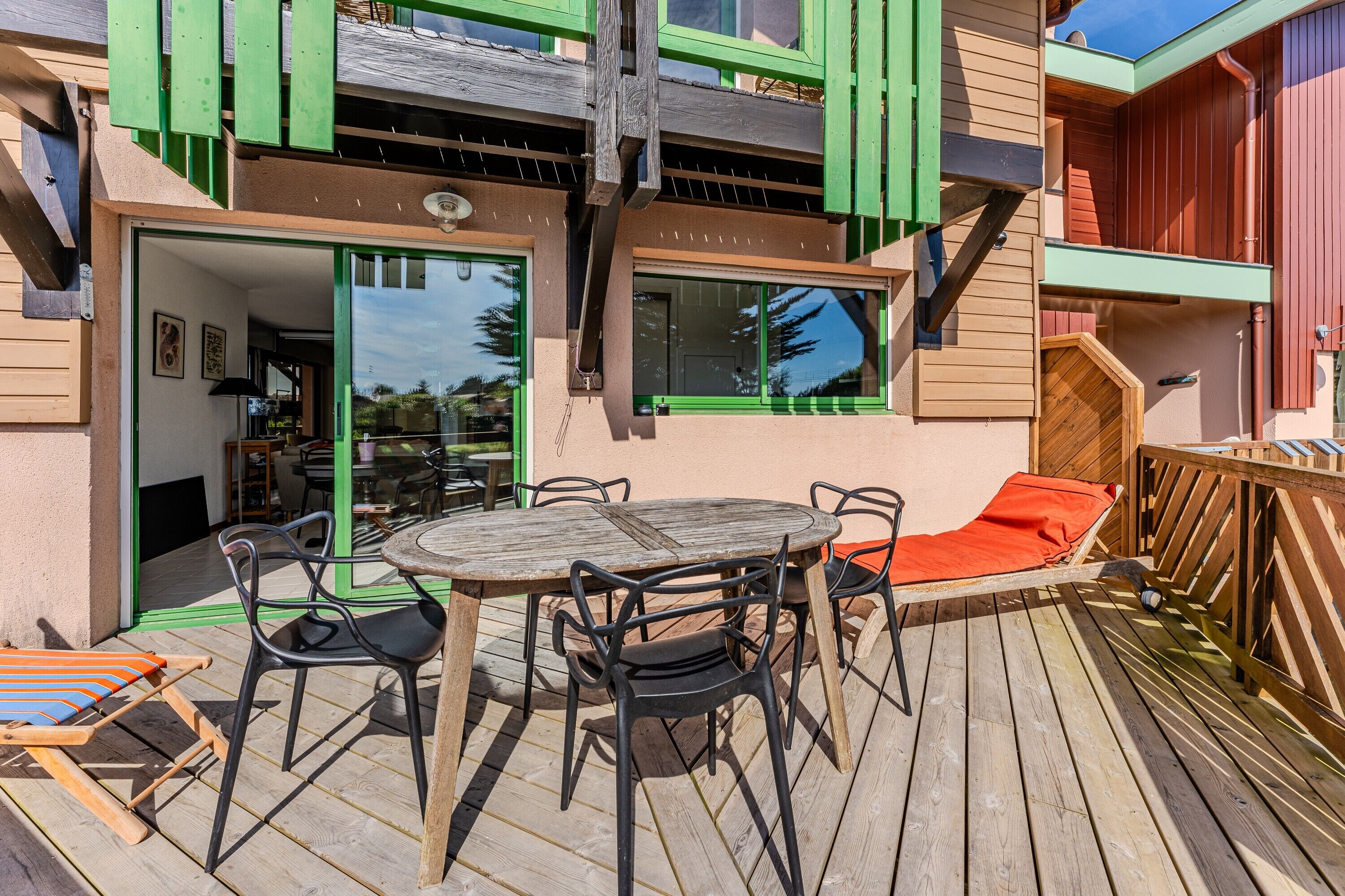 Une terrasse en bois avec une table ronde et des chaises, un fauteuil de relaxation rembourré et une clôture en bois.