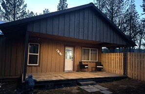 A wooden cabin with a front porch, a door, and two windows.