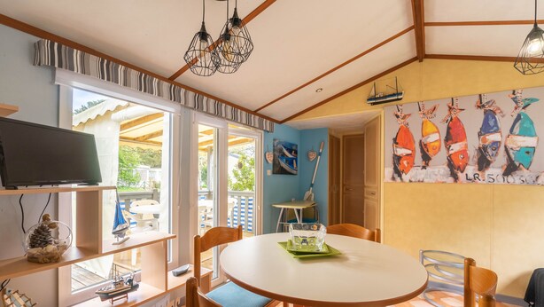 Ein Essbereich mit einem runden Tisch, Stühlen, einem Fernseher auf einem Regal und einem Wandgemälde mit Fischen.