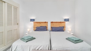 Habitación con dos camas, cada una con cabecero de madera, dos lámparas de noche y toallas dobladas sobre las camas.