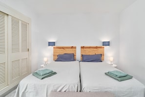 A room with two beds, each with a wooden headboard, two bedside lamps, and folded towels on the beds.