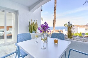 Une terrasse avec une table, des chaises et des boissons, donnant sur une plage et des palmiers.