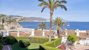 Un pueblo costero con una palmera destacada, edificios de tejas rojas y vista al mar.