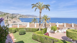 Una propiedad costera con camino de entrada pavimentado, palmeras y vista al mar.