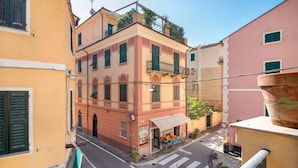 A narrow street with buildings on either side, a visible storefront with outdoor seating, and a pedestrian crossing. - Apartment 'Piter' with Private Terrace (Bonassola)