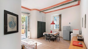 A room with a dining table, chairs, a red pendant light, a refrigerator, and a bed with a floral bedspread. - Apartment 'Piter' with Private Terrace (Bonassola)