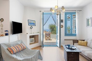 A living room with a sofa, a chair, a television, a table with a tray, and a view through a door.