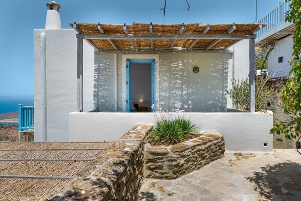 A white building with a blue door, a stone wall, and a view of the sea.