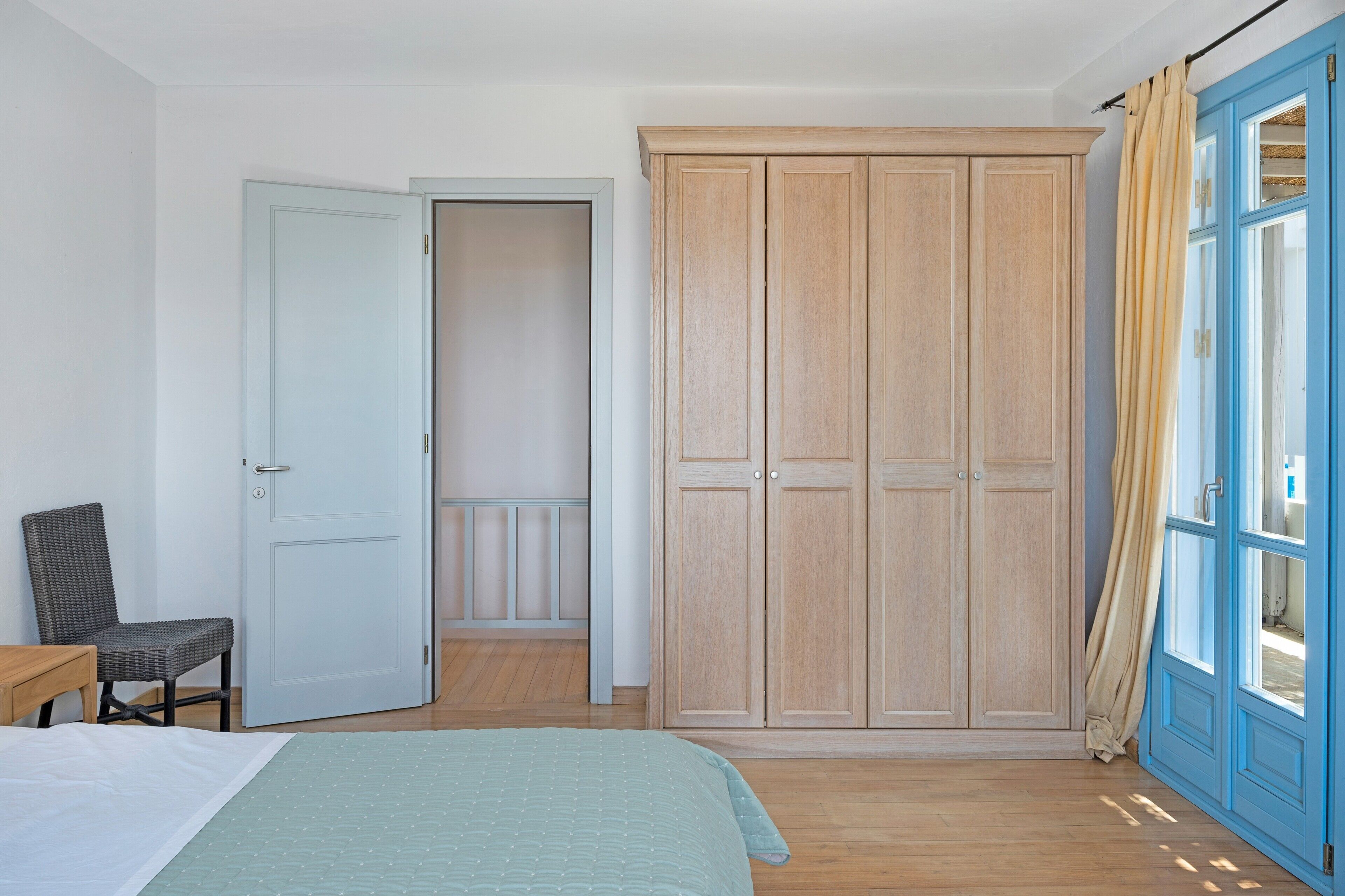 A bedroom with a bed, a chair, a wardrobe, and a door leading to another room.