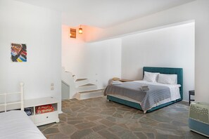A bedroom with a bed, a nightstand, a suitcase, a staircase, and a wall-mounted light fixture.