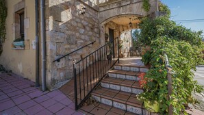 Un edificio de piedra con una escalera que lleva a la entrada, una pequeña ventana con una planta y una maceta con planta en los escalones.