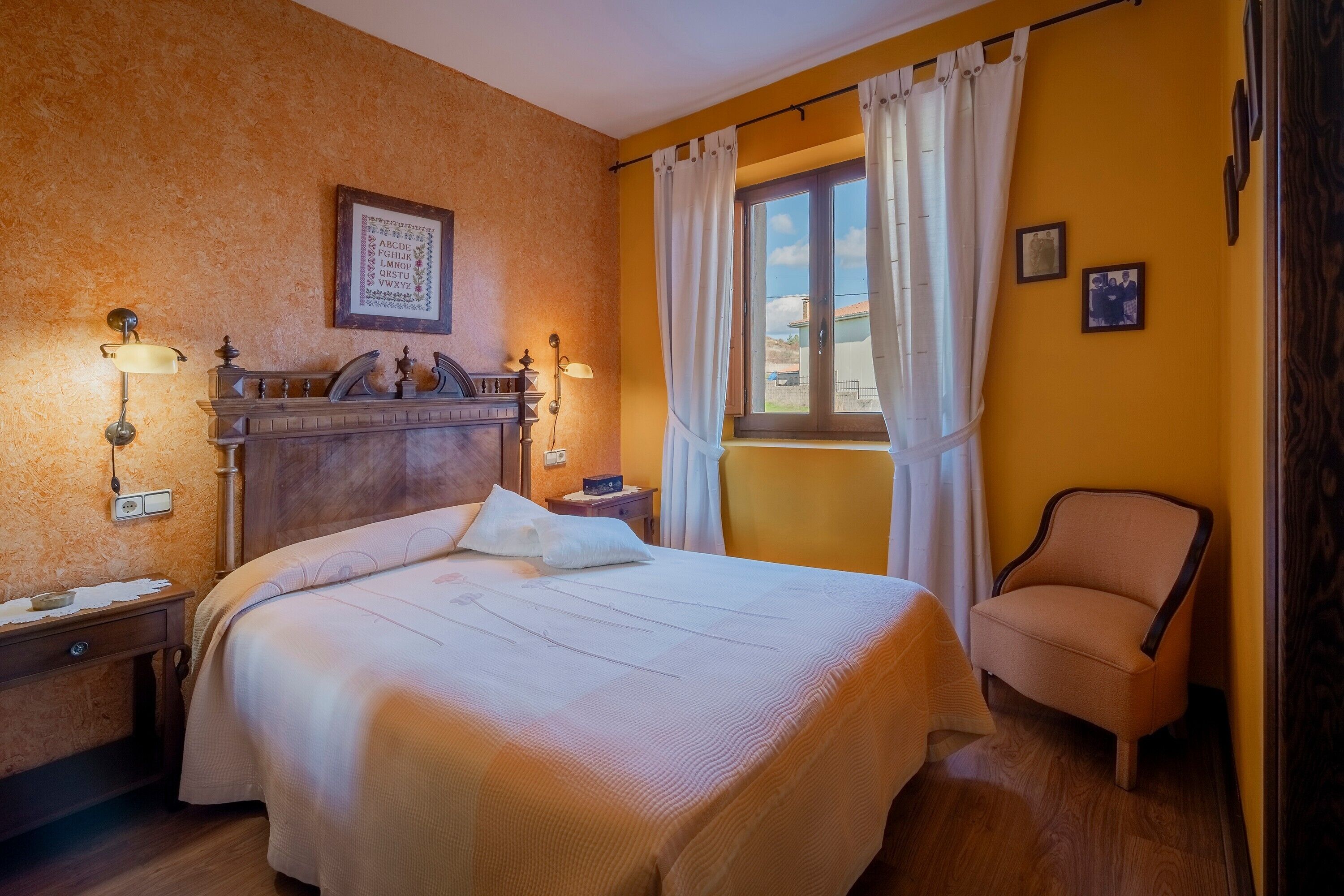 A hotel room with a bed, a chair, a nightstand, a lamp, a window with curtains, and a wall-mounted picture.