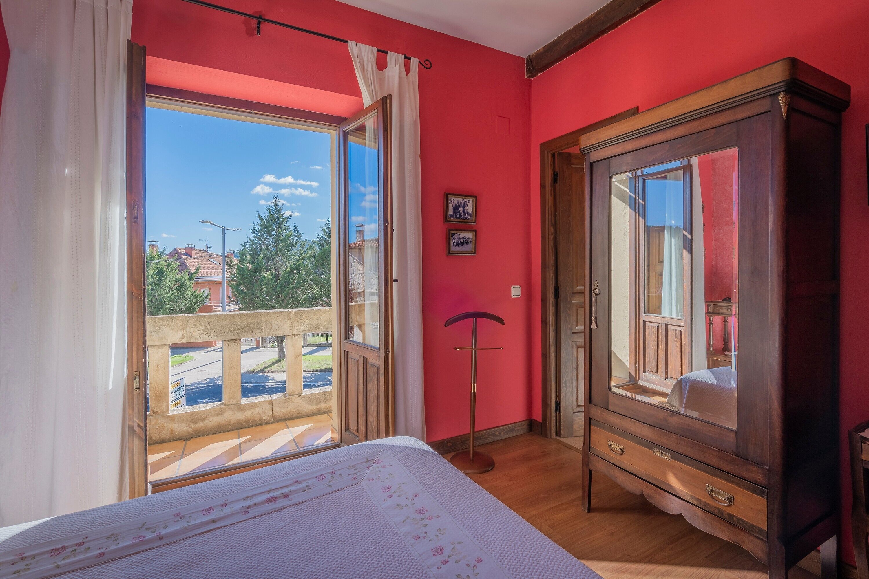 A bedroom with a bed, a wooden wardrobe, a standing lamp, and a balcony with a view of the outside.