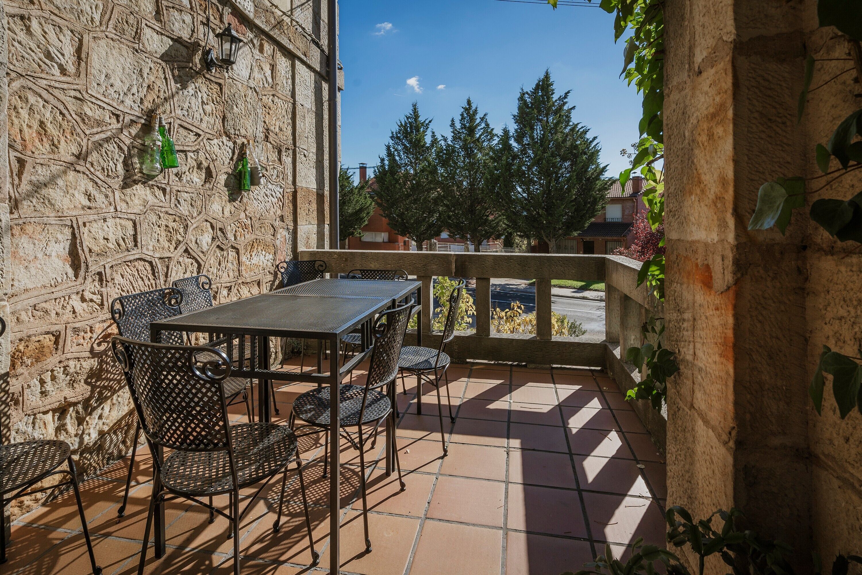 A stone wall with metal furniture, a tiled floor, and a view of trees and houses.