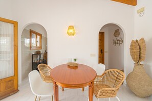 A dining area with a round wooden table, wicker chairs, and a wall-mounted light fixture. - Holiday Home 'Villa Mellizo' with Private Pool, Wi-Fi and Air Conditioning (El Campello)