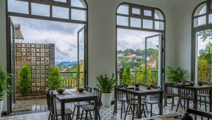 A restaurant with outdoor seating, large windows, and a view of a hilly landscape. - The Gate Boutique Hotel Da Lat (Xuan Huong - Da Lat)