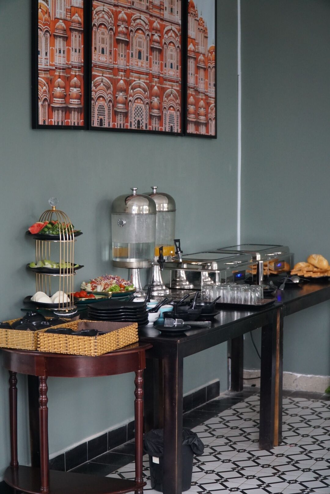 Een buffetopstelling met diverse gerechten, een decoratieve vogelkooi en een schilderij van een gebouw aan de muur.