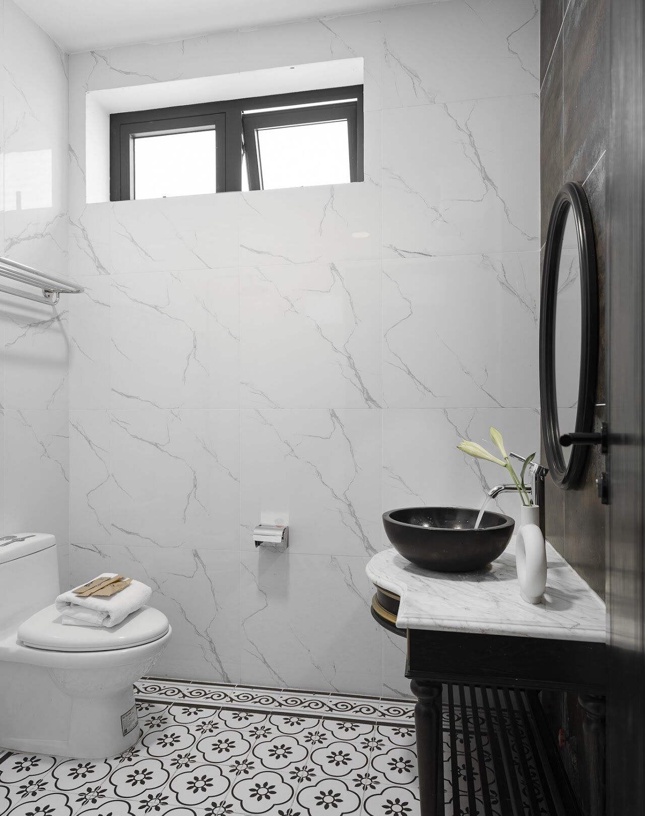 A bathroom with a toilet, a sink with a bowl, a mirror, and a window above the toilet.