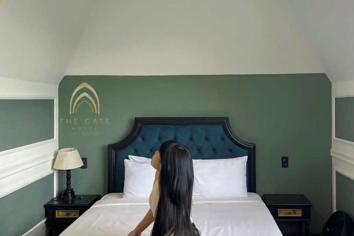 A hotel room with a large bed, a headboard, a nightstand with a lamp, and a wall-mounted sign.